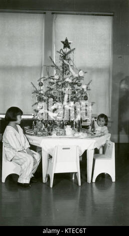 Children on the Rosebud Indian Reservation in South Dakota sit at a table which holds a Christmas tree with a toy train set which encirlces it. Stock Photo