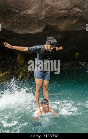 Boy standing on shoulders of another, forming a human tower in a pool of water at Nagarmadi Water Falls, Chendia, Karnataka, India Stock Photo