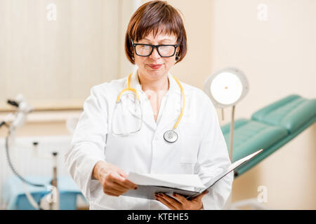 Portrait of a senior woman gynecologist standing in the office with gynecological chair and lamp on the background Stock Photo