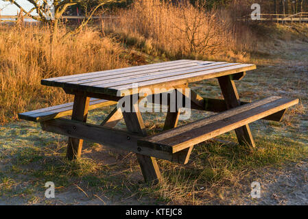 Wooden outdoor bench and table on a cold morning. Frost cover the wooden surface. The morning sunshine has started to thaw the ice. Stock Photo