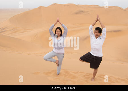 An Indonesian girl and Filipino boy doing a yoga tree on Dune 7, the highest sand dune in the world, in Walvis Bay, Namibia Stock Photo