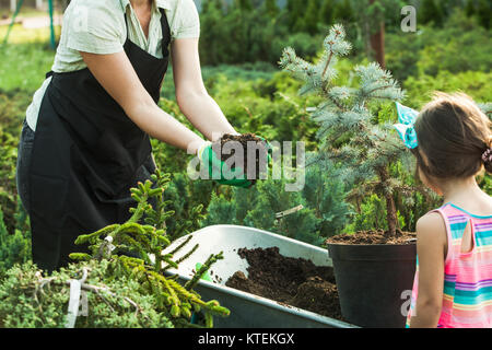 Young woman gardener shows a girl transplanting a plant in fertile soil Stock Photo