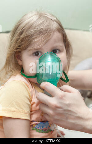 Young child doing inhalation with a nebulizer at home. Mother hands holding mask Stock Photo