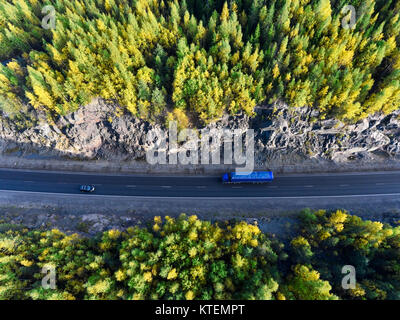 Top view at blue semi-trailer truck driving between rock tunnel in autumn green and yellow forests of Karelia, Russia Stock Photo
