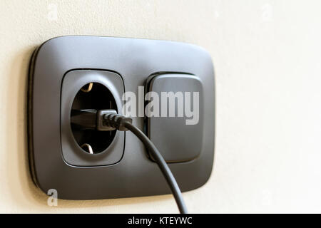 Black power cord cable plugged into european wall outlet on white plaster wall Stock Photo