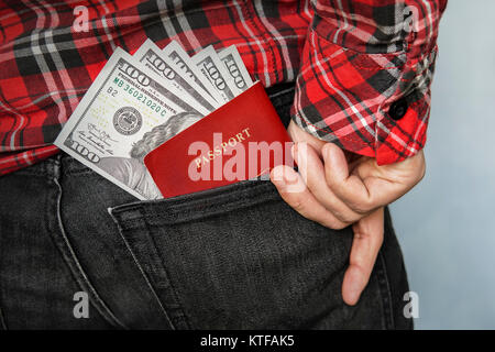 Man gets money and a passport from the back pocket of black jeans. Out of pocket expenses. Currency exchange. Bills of American money in denominations Stock Photo