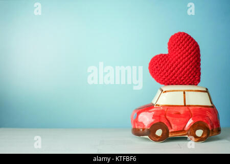 Miniature red car carrying a red heart on cyan background Stock Photo