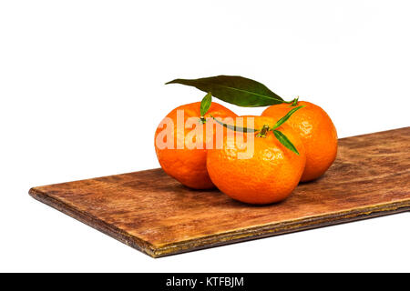 On a wooden surface lie three ripe orange mandarins with green leaves closeup Stock Photo
