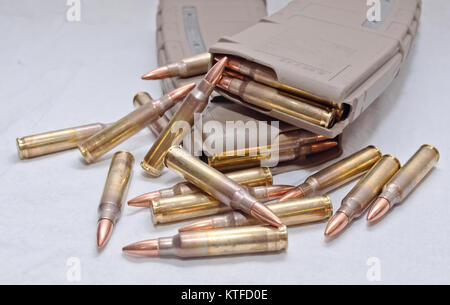 Two brown rifle magazines loaded with .223 rounds and several rounds laying next to them on a white background Stock Photo