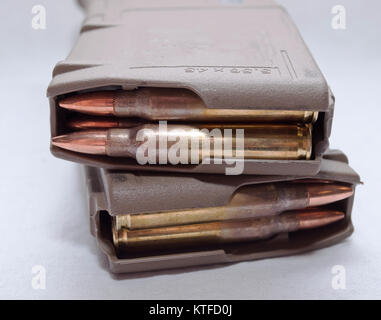 Two loaded .223 rifle magazines stacked on top of each other on a white background. The magazines are stacked in opposite directions from one another. Stock Photo