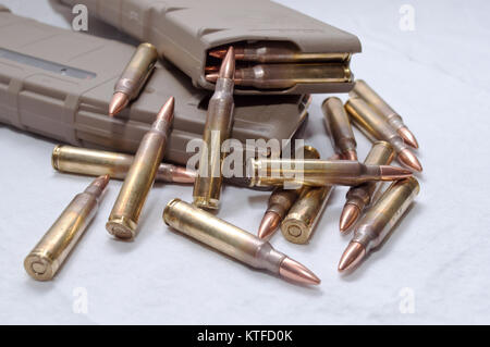 Two brown rifle magazines loaded with .223 rounds and several rounds laying next to them on a white background Stock Photo