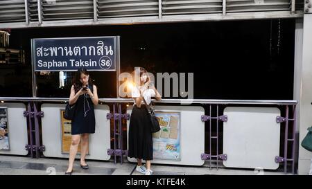 2 Ladies Waiting for Train BTS Skytrain Saphan Taksin Station Bangkok Thailand dec 2017 Stock Photo