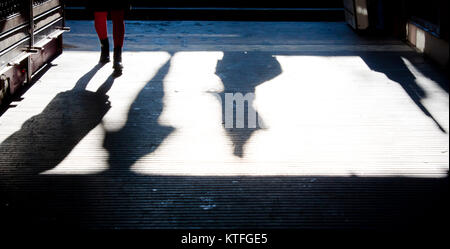 Teenage girl in red tights approaching with a shadow in the subway passage , and other people shadows going down the stairs to underground walkway Stock Photo