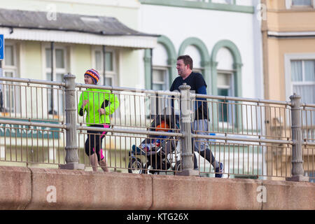 Hastings, East Sussex, UK. 26th December 2017.  Lots of people out and about enjoying the mild boxing day weather this morning. This couple take the pushchair for of a jog as well. Photo Credit: Paul Lawrenson/ Alamy Live News Stock Photo