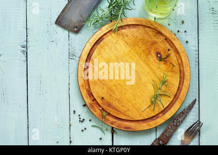 Culinary background. Cutting board, various spices and rosemary on a wooden kitchen table. Flat lay, top view with copy space. Stock Photo