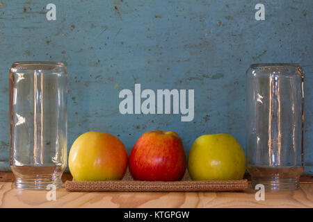 Three colored apples on a linen napkin between the glass jars on the background of old blue wall. Free space for text. Copy space. Rustic concept Stock Photo