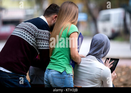 Group of young people using laptop and tablet on a park bench, having fun, talking, hanging out Stock Photo