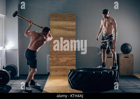 Sledgehammer Tire Hits men workout at gym with hammer and tractor tire Stock Photo