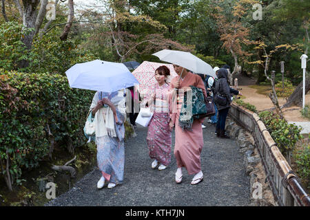 JAPAN, KYOTO-CIRCA APR, 2013: Three geishas wearing traditional japanese kimono are on pathway in Kinkaku-ji temple park. Women walking with umbrellas Stock Photo