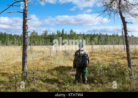 Man with backpack and bucket standing in front of wet swamp, lost in woods Stock Photo