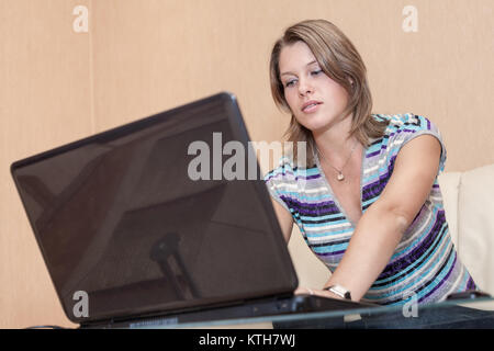 Young Caucasian woman sitting on sofa with laptop on table, looking at screen Stock Photo