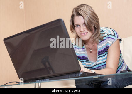 Young Caucasian woman watching screen with smile on face, using laptop at home Stock Photo