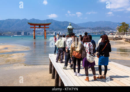 ITSUKUSHIMA, JAPAN-CIRCA APR, 2013: Group of Japanes people stands on pier of Itsukushima Shrine and looks at the great Torii in bay at low tide water Stock Photo