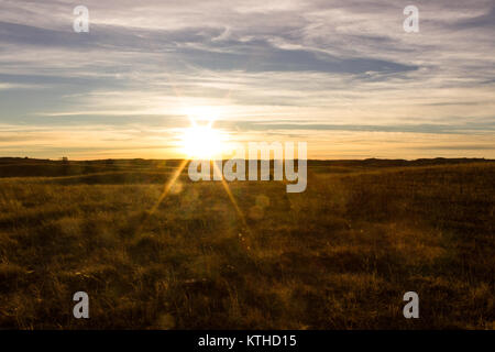 The sun sets behind the Sandhills of North Central Nebraska, casting a warm glow over the gently rolling hills. Stock Photo