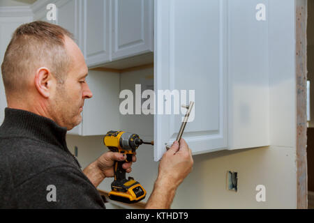installation of door handles on kitchen white cabinet with a screwdriver Stock Photo