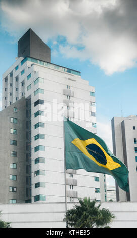 Brazilian flag on a pole with a modern buidling on background and blue sky with clouds Stock Photo