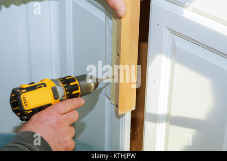Worker use drill to repair furniture and drills the cabinet door a cordless screwdriver, close up. Stock Photo
