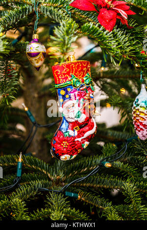 Traditional colourful shiny red Santas Claus (Father Christmas) glass decoration in the shape of a stocking hanging on a Christmas tree, England, UK Stock Photo