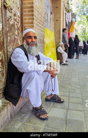 Yazd, Iran - April 22, 2017: Muslim in Islamic attire sits on threshold of house in front of sidewalk. Stock Photo