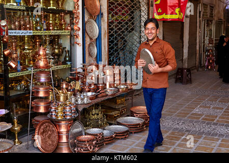 Yazd, Iran - April 22, 2017: A young smiling man walks past a shop with copper utensils, holding a metal tray in his hands. Stock Photo