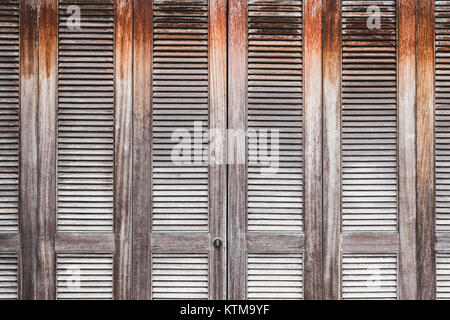Old shabby wooden door with jalousie shutter. Grunge wall background Stock Photo