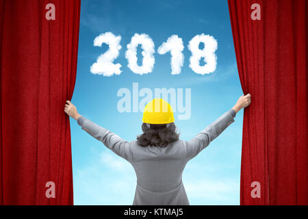 Architect woman opening red curtain with 2018 number on the sky background Stock Photo
