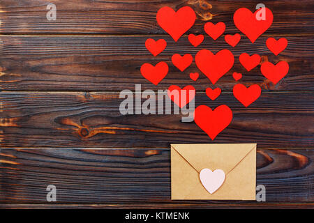 Valentine day love letter. Envelope from craft paper with red hearts heap spread on black wood background. Letter to Valentine Day. Stock Photo