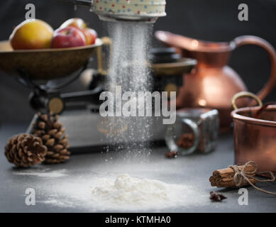 flour Sprinkled on a black table with anise stars, pine cones, apples, and vintage scale Stock Photo