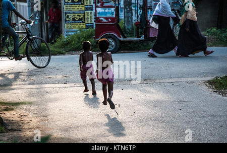 Two kids and two women in veils walk past a city street. of Khulna Stock Photo