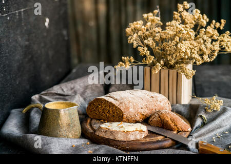 Close up rye bread with butter sandwich, knife, mug with coffee and dry flowers in vase -- beautiful breakfast image on dark background Stock Photo