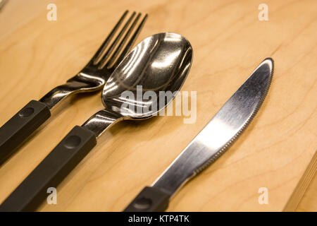 Close up silverware set of spoon, knife and fork with black plastic handles lying on table Stock Photo