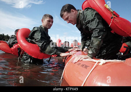 HOMESTEAD, FL - Major Dave Sumwalt pulls Captain Lonnie Mazuranich, both members of the 101st Rescue Squadron, aboard a survival raft during Water Survival Training (WST) near Homestead Air reserve Base on January 20, 2016. During this training, members train on the use of seven and twenty man survival rafts, the ability to work as a team in open water, and the use of their survival equipment. Additionally, aircrew members must conduct multiple dunks in the Shallow Water Egress Trainer in a four foot, man-made pool, and demonstrate an ability to exit an aircraft while upside down and completel Stock Photo