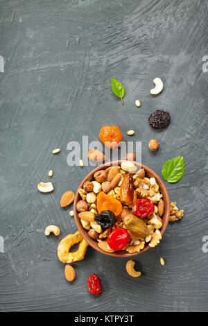 Various dried fruits and nuts in a ceramic bowl (walnut, cashew, almonds, pine nuts, hazelnuts) on a gray stone or slate background. The concept of a  Stock Photo