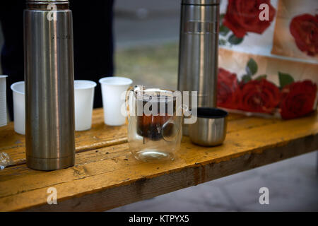 Close up wooden table with small transparent teapot, thermoses and plastic glasses for drinking tea in street Stock Photo