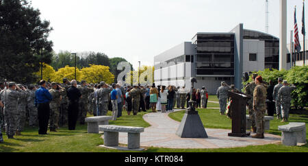 LATHAM, N.Y -- Employees, Soldiers, Airmen and others render honors during a Memorial Day ceremony held at the New York State Division of Military and Naval Affairs (DMNA) here on May 26. Over 100 people attended the ceremony, which was held on DMNA grounds near the New York Military Forces Memorial (center). The memorial depicts an inverted rifle and bayonet with helmet displayed inside a pair of combat boots, most often referred to as a battlefield cross. (U.S. Army National Guard photo by Master Sgt. Raymond Drumsta, 42nd Infantry Division/released) Stock Photo