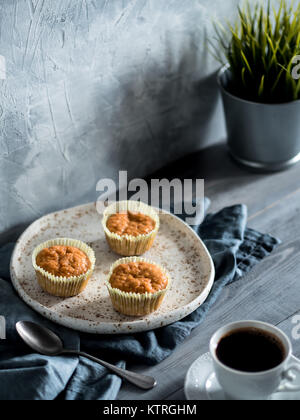 Homemade muffins on craft plate and coffee cup over gray wooden table. Carrot cupcakes with copy space. Toned image in scandinavian style. Stock Photo