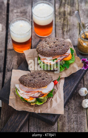 rye sandwiches with ham and letucce on wood table with two glasses of beer Stock Photo