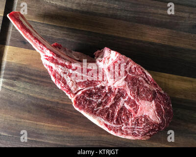 Close up of raw beef meat. Tomahawk ribeye steak, bone-in, on wooden cutting board. Stock Photo