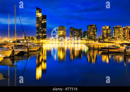 Dark colourful sunset over Docklands suburb in Melbourne on waterfront of Yarra river with marina for yachts. Bright illumination reflects in still wa Stock Photo