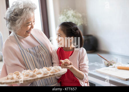Cheerful granddaughter and grandmother making dumplings in kitchen Stock Photo